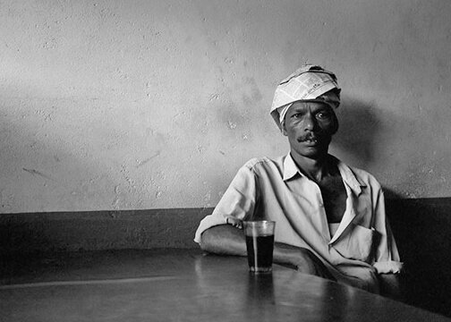 A man sitsing on a chair with a glas in front of him